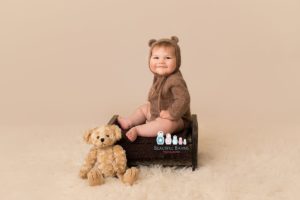 professional baby portrait photo of baby boy in teddy bear outfit sat on wooden bench with teddy bear by baby photographer Beautiful Bairns Photography