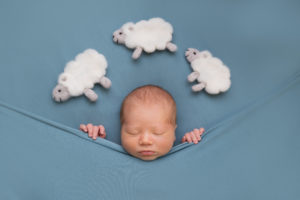 professional newborn photo of newborn baby tucked in laying on teal fabric with fluffy sheep above his head by newborn photographer edinburgh beautiful bairns
