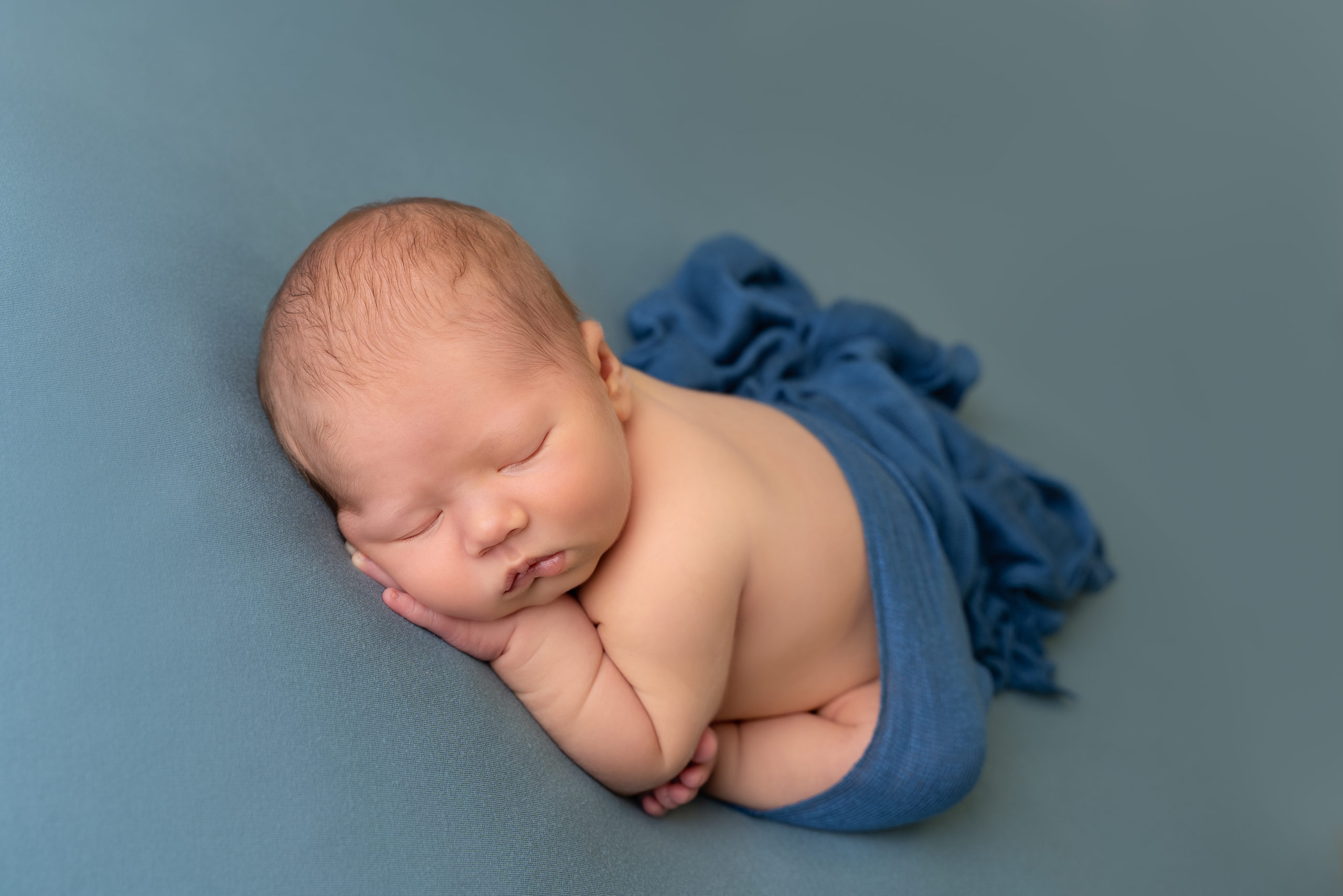 newborn baby photo of baby boy on teal blanket with teal wrap draped over his bottom by newborn photographer edinburgh Beautiful bairns Photography