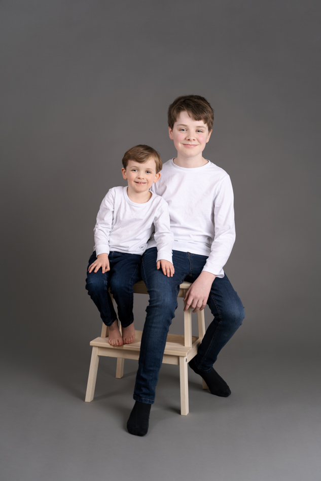 professional portrait of two boys wearing white shirts and denim jeans in front of a grey backdrop. Photograph by Beautiful Bairns photography Edinburgh family photographer