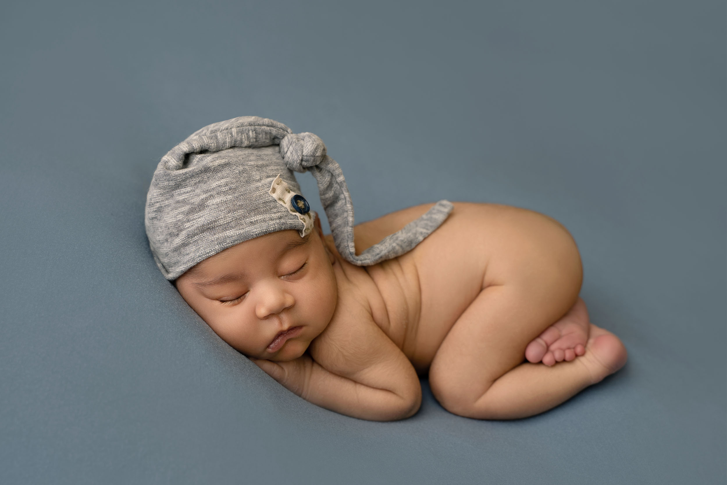 photograph of newborn baby boy posed on blue fabric with grey hat
