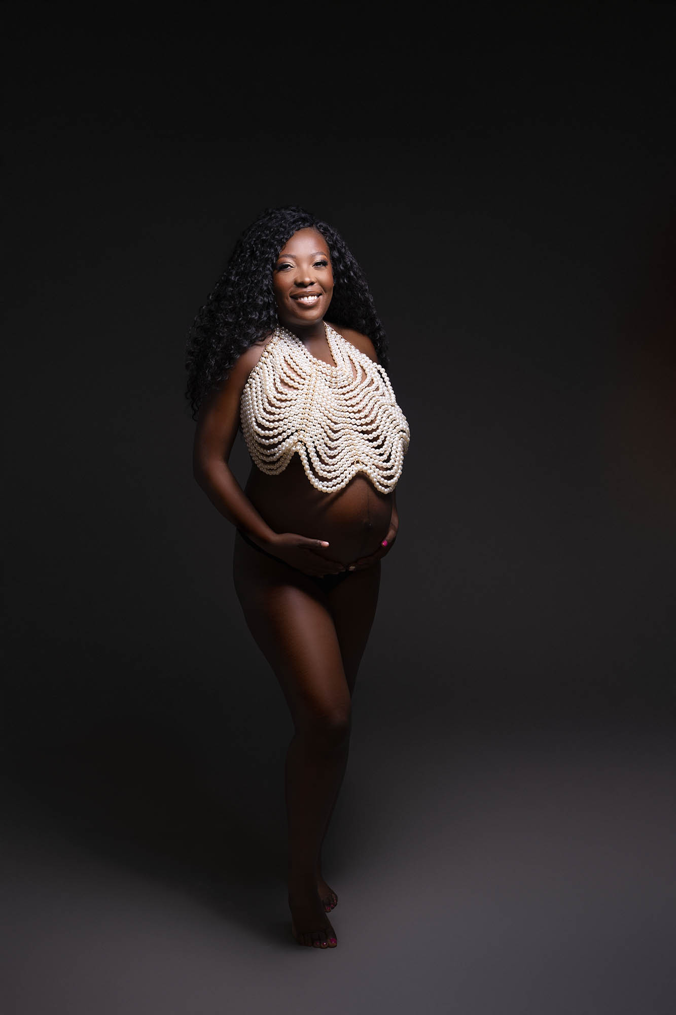 professional maternity photo of a pregnant woman posed wearing a large pearl necklace covering her chest sitting above her pregnant belly by maternity photographer Beautiful Bairns photography