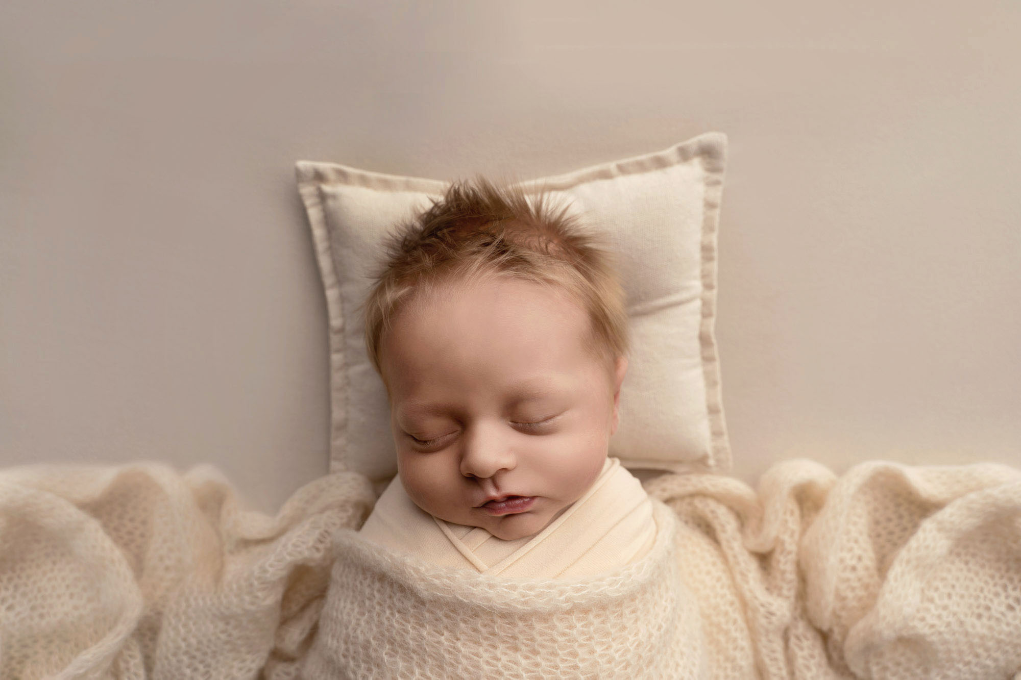 Newborn photographer Edinburgh - colour photograph of newborn boy wrapped in a swaddle with a small pillow underneath his head taken by Edinburgh newborn photographer Beautiful Bairns Photography