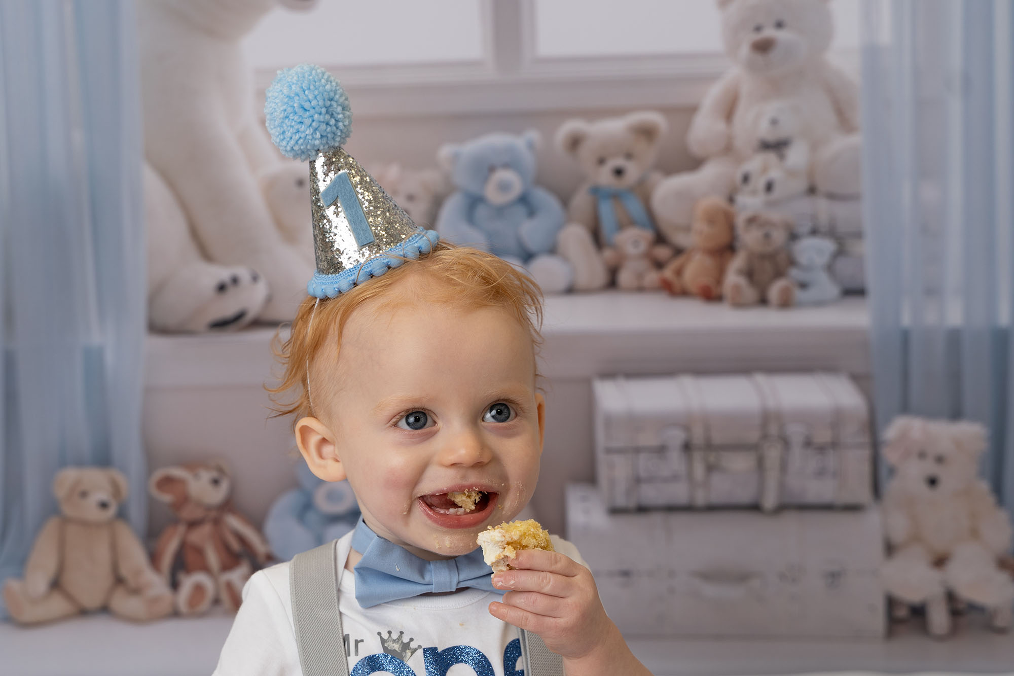 cake smash photo of little girl celebrating 1st birthday with a rainbow themed cake smash with rainbow cake and rainbow paper fans behind her by cake smash photographer beautiful bairns photography edinburgh