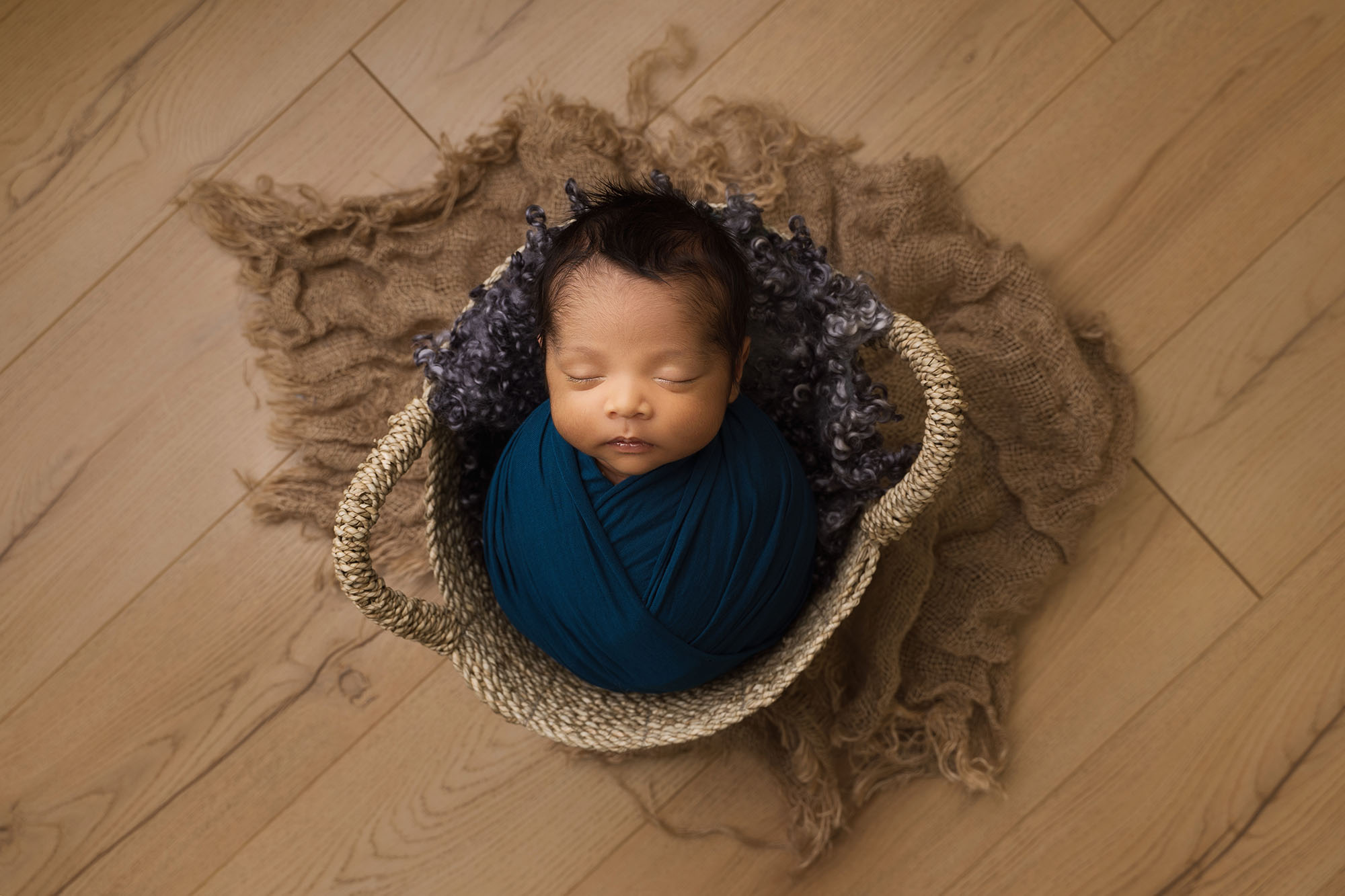 photo of newborn baby photographed laying in a basket with jute underneath wrapped in a navy swaddle during his newborn session by edinburgh newborn photographer beautiful bairns