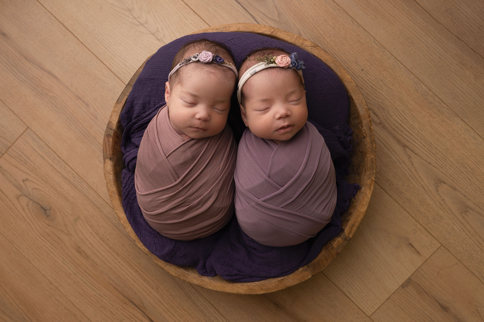 newborn baby twins wrapped in purple swaddles in a wooden bowl by newborn photographer edinburgh