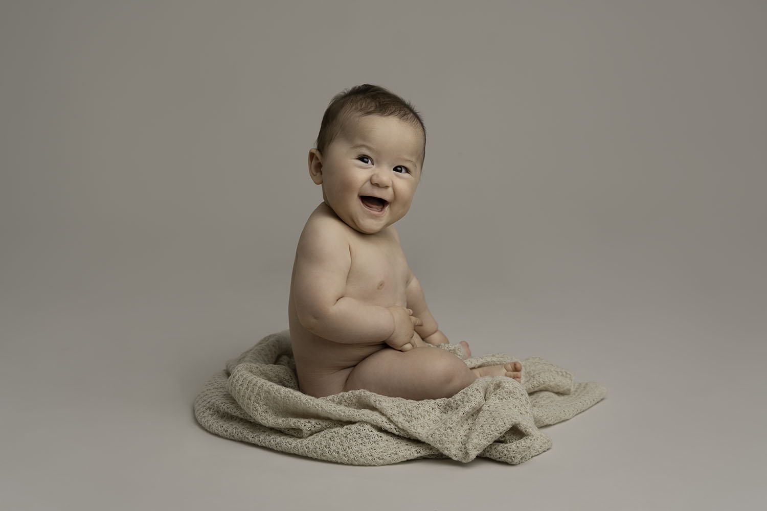 photo of a naked 8 month old baby sitting on textured fabric smiling to camera by baby photographer edinburgh beautiful bairns photography